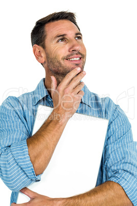 Thoughtful young man with hand on chin holding laptop