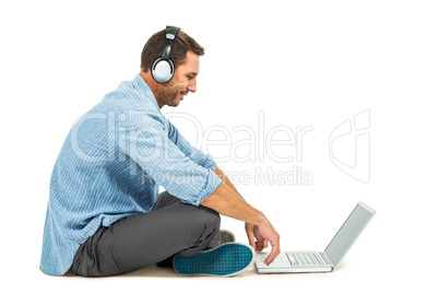 Smiling man sitting on floor using laptop and headphones