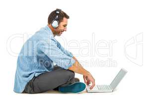 Smiling man sitting on floor using laptop and headphones