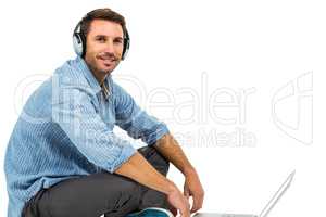 Portrait of man sitting on floor using laptop and headphones