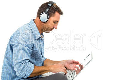 Young man sitting on floor using laptop and headphones