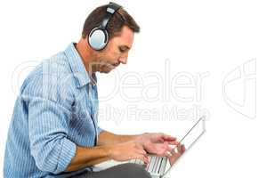 Young man sitting on floor using laptop and headphones