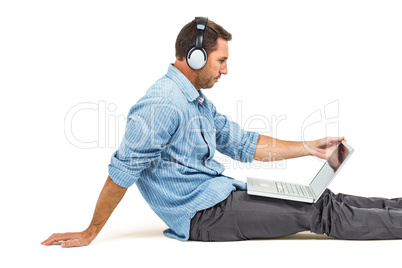 Man sitting on floor using laptop and headphones