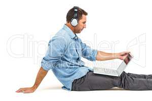 Man sitting on floor using laptop and headphones