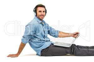 Happy man sitting on floor using laptop and headphones