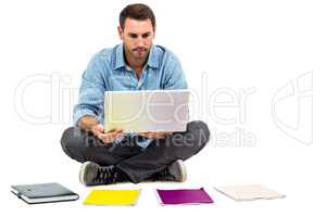 Man sitting on floor using laptop with notepads on floor