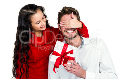 Smiling woman covering eyes of partner holding gift
