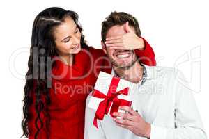 Smiling woman covering eyes of partner holding gift