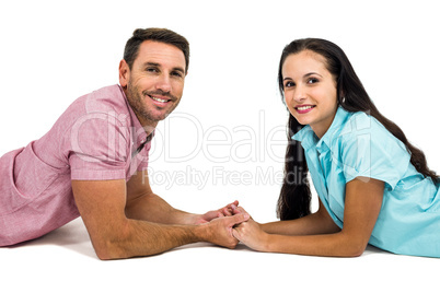 Happy couple laying on the floor face to face holding hands