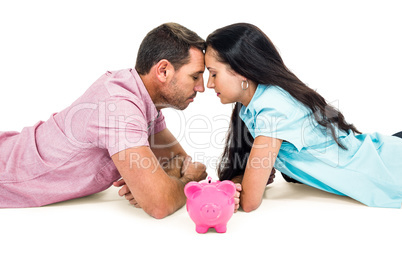 Couple laying on the floor face to face with piggybank
