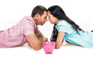 Couple laying on the floor face to face with piggybank