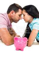 Young couple laying on the floor face to face with piggybank