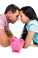 Worried couple laying on the floor face to face with piggybank