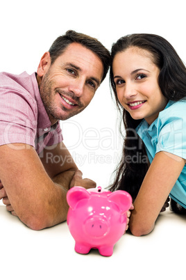 Smiling couple laying on the floor face to face with piggybank