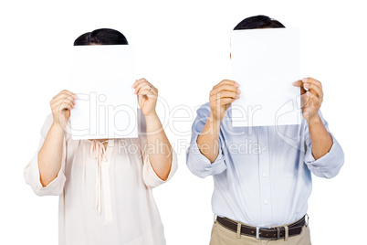 Couple holding pages over faces