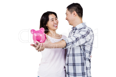 Happy couple looking at each other while holding piggy bank