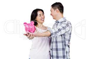 Happy couple looking at each other while holding piggy bank