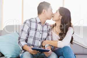Couple kissing and holding digital tablet at home