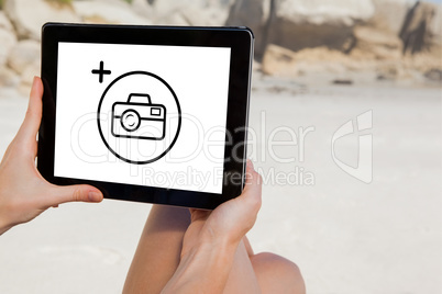 Composite image of woman sitting on beach using tablet pc