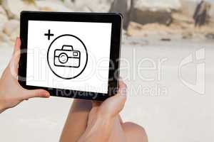 Composite image of woman sitting on beach using tablet pc
