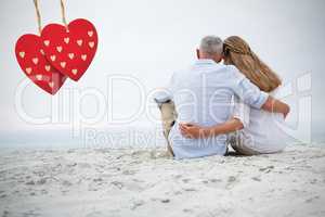 Composite image of happy couple sitting on the sand and looking