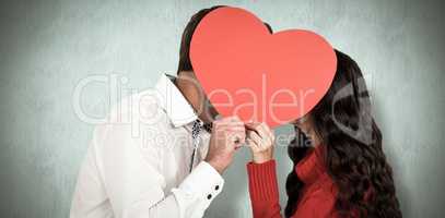 Composite image of couple covering faces with paper heart