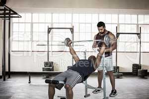 Composite image of trainer helping muscular man to lift the barb