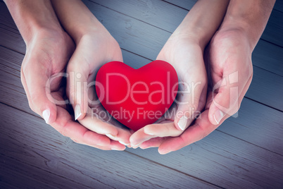 Composite image of couple holding miniature heart in hands