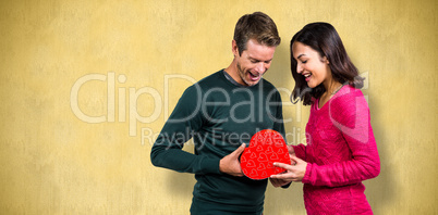 Composite image of happy young couple with heart shape gift