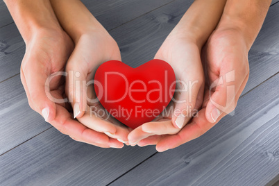 Composite image of couple holding miniature heart in hands