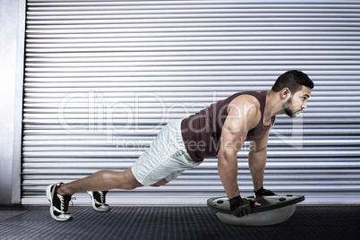 Composite image of muscular man doing bosu push ups