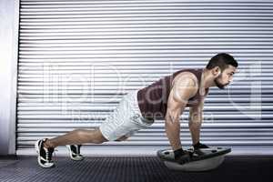 Composite image of muscular man doing bosu push ups