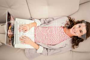 Composite image of woman using laptop while lying on sofa at hom