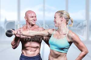 Composite image of cheerful trainer helping woman for lifting du