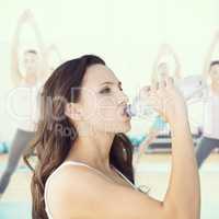 Composite image of beautiful woman drinking water from bottle