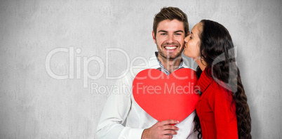 Composite image of man holding paper heart and being kissed by g