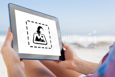 Composite image of woman sitting on beach in deck chair using ta