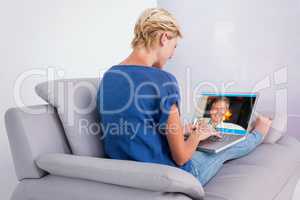 Composite image of blonde woman using her laptop on the couch