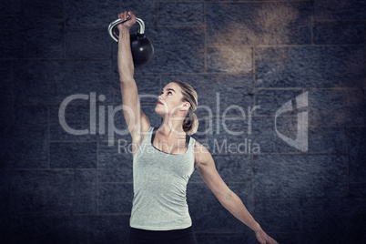 Composite image of serious muscular woman lifting kettlebell