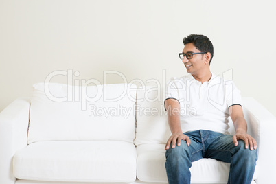 Lonely single Asian man sitting on couch and looking at side