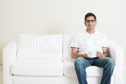 Asian man sitting on couch and drinking coffee