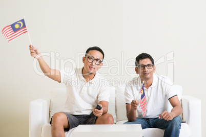 Malaysian men with Malaysia flag watching sports on tv