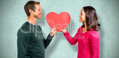 Composite image of smiling couple holding red heart shape