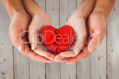 Composite image of couple holding broken heart in hands