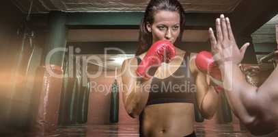 Composite image of female boxer with fighting stance against trainer hand