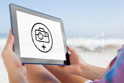 Composite image of woman sitting on beach in deck chair using ta