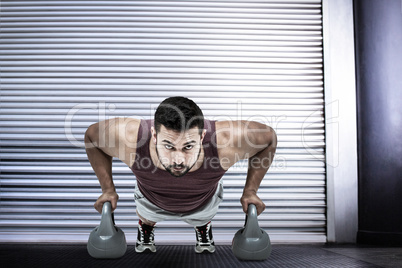 Composite image of muscular man doing push ups with kettlebells