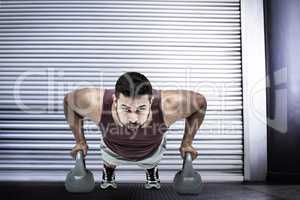 Composite image of muscular man doing push ups with kettlebells