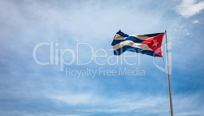 Cuban flag flying in the wind on a backdrop of blue sky.