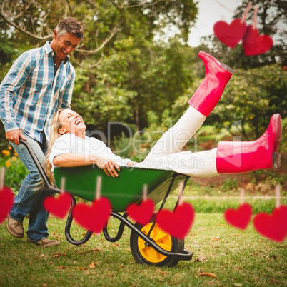 Composite image of happy couple playing with a wheelbarrow